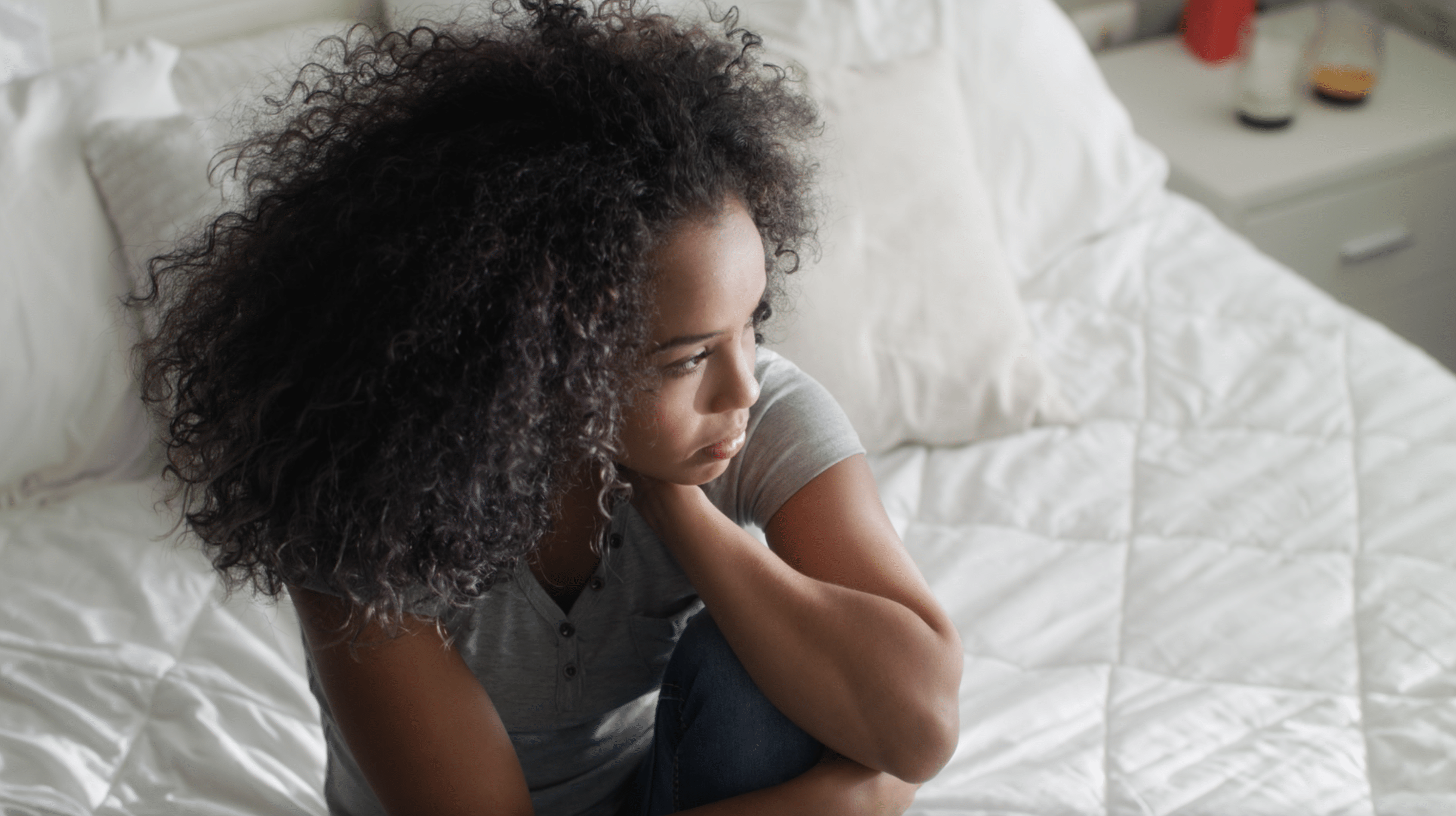 teenage girl sitting on her bed upset