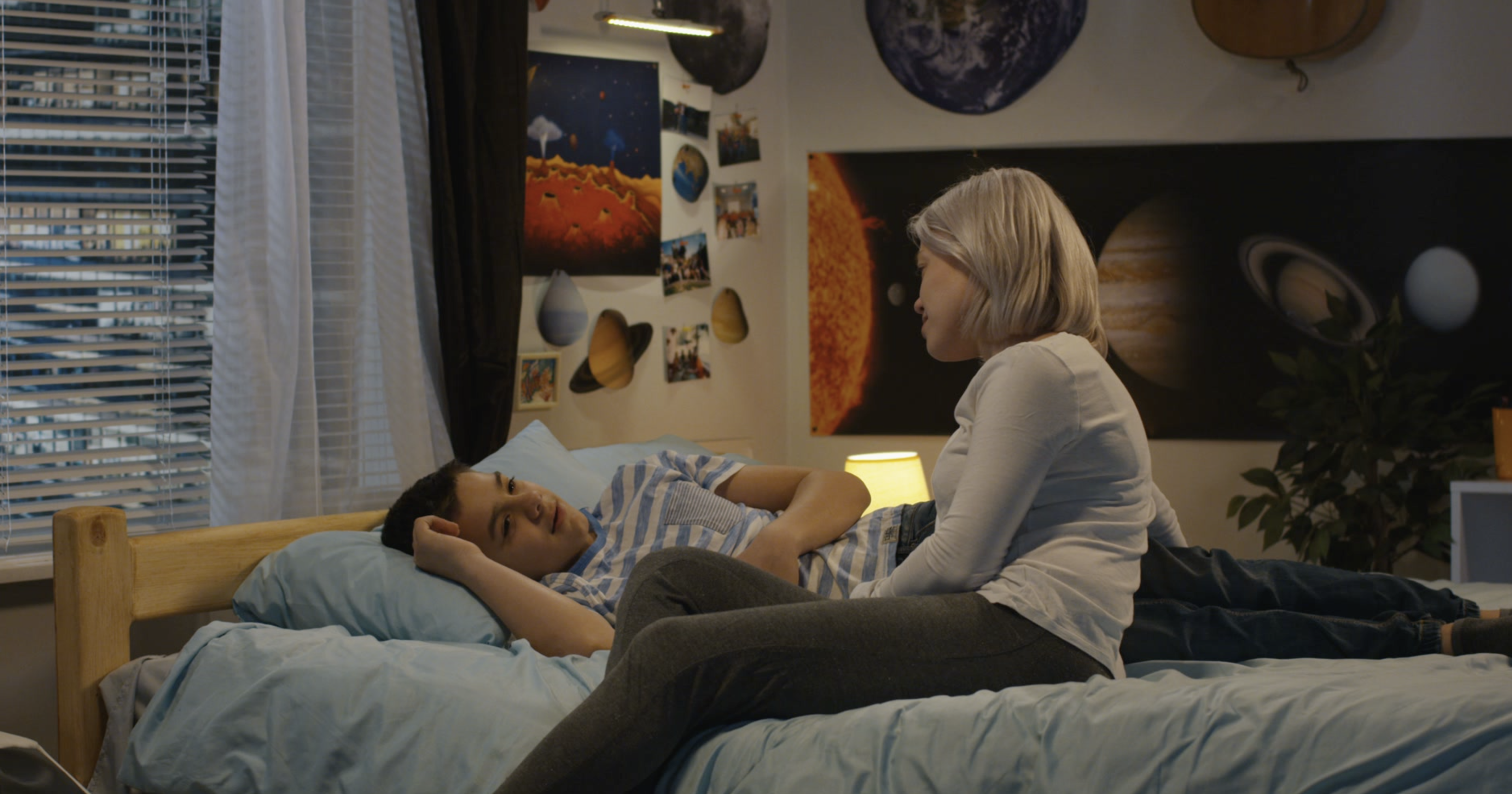 Mother talking to distressed son lying on his bed