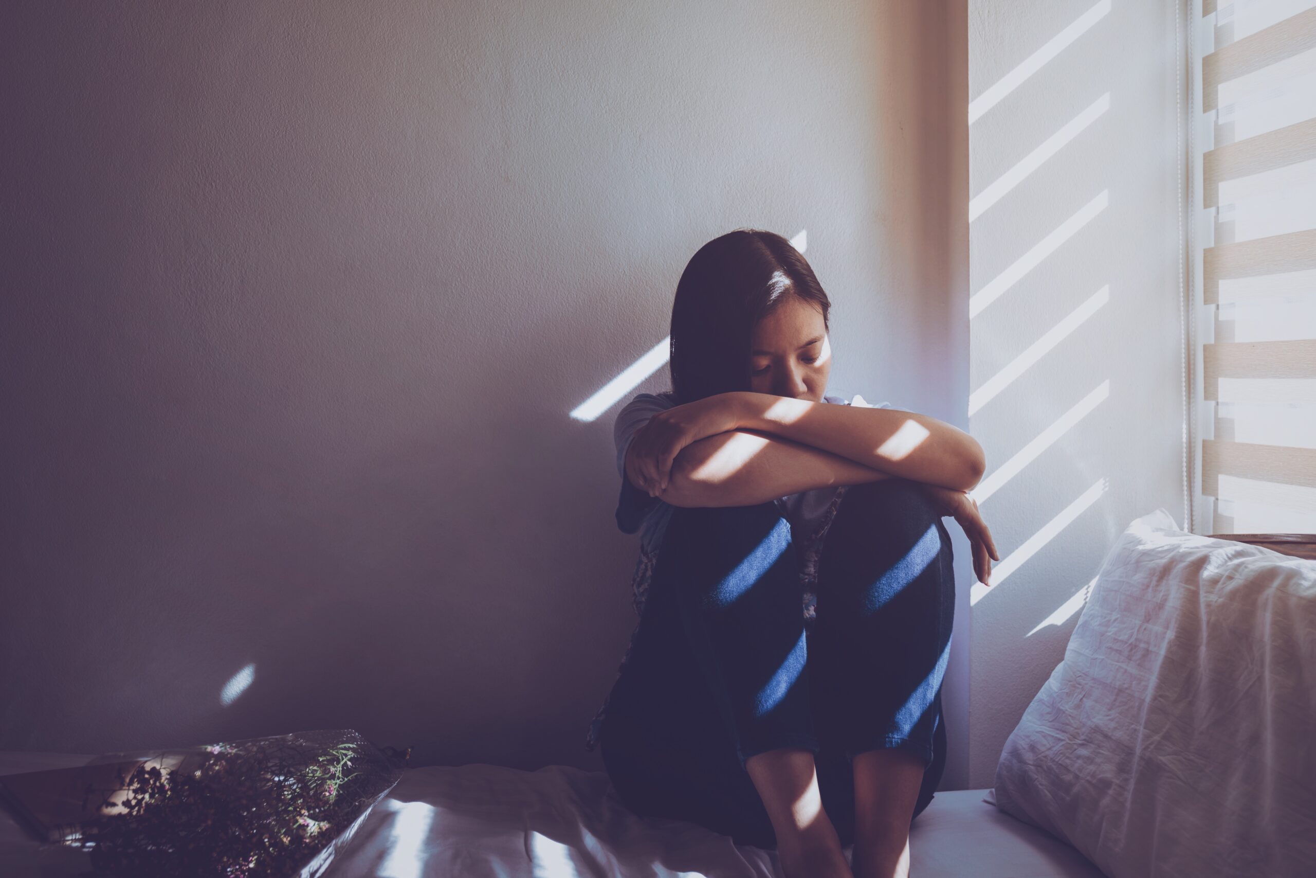 woman sat on her bed with her head on her knees