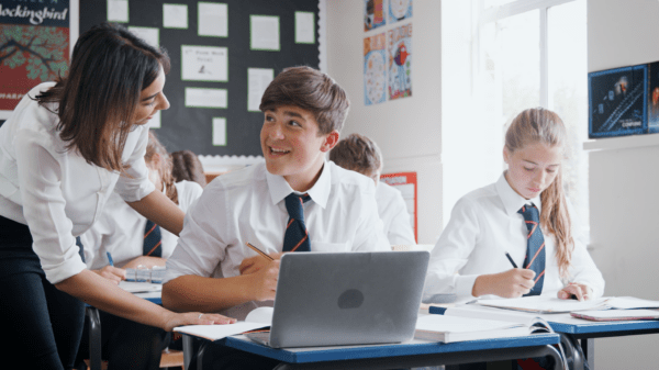 boy talking to his teacher in school uniform with laptop in front of him