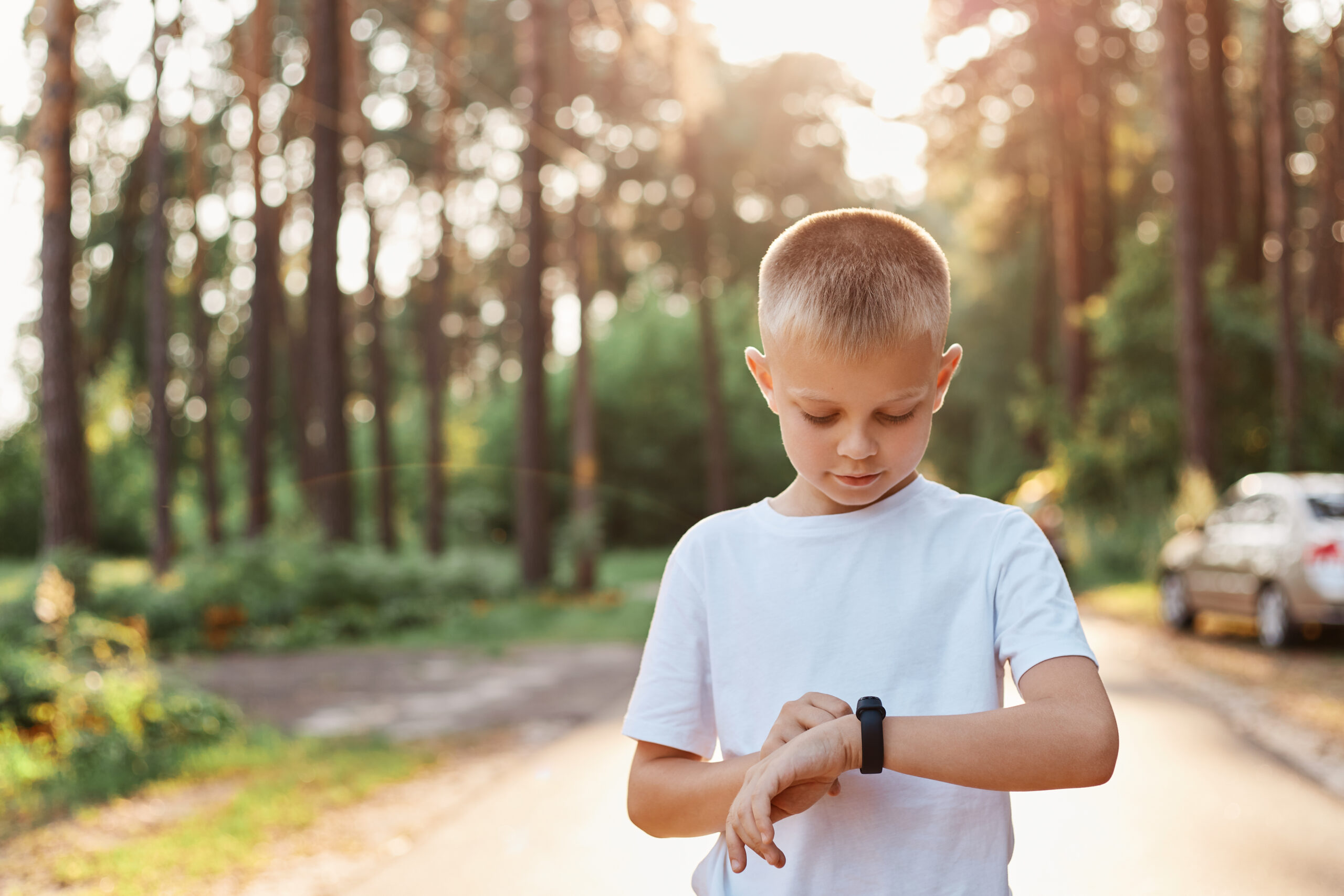 Little blonde boy using fitness bend touching button and touchscreen while posing outdoor in park